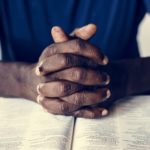 African American male hands resting on an open bible